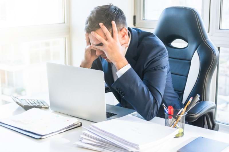 A businessman sitting at his work desk is feeling irritability as a symptom of caffeine withdrawal.