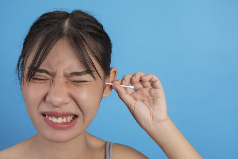 A young woman is trying to use a Qtip to remove her excess ear wax buildup