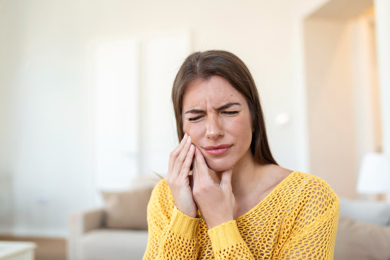 A woman is in noticeable pain as she is holding the right side of her jaw.  The pain is coming from her temporomandibular joint.