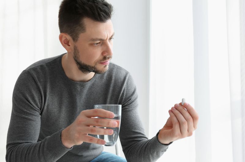 A man is examining a white medicine pill that he is about to take with water