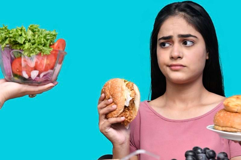 A young girl eating junk food but avoiding to eat healthy green balanced diet.