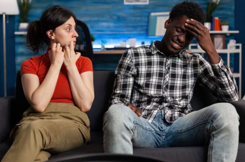 An interracial couple sitting on the sofa all stressed out from fighting.