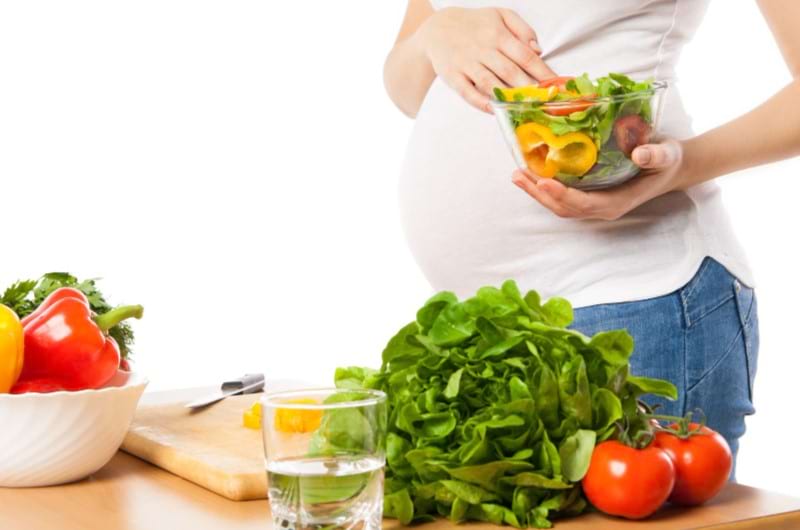 A pregnant woman is holding a bowl full of veggies rich in folic acid and good for the baby and pregnancy.