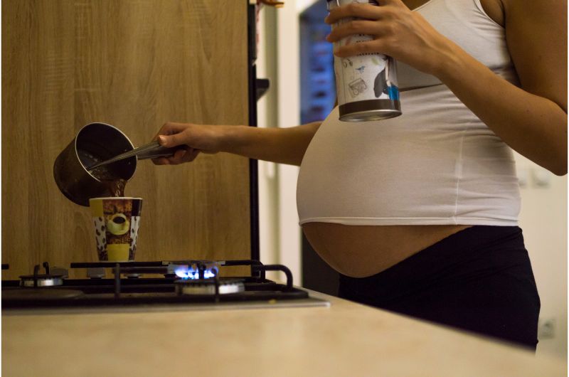 A pregnant woman is pouring herself a cup of hot coffee at home