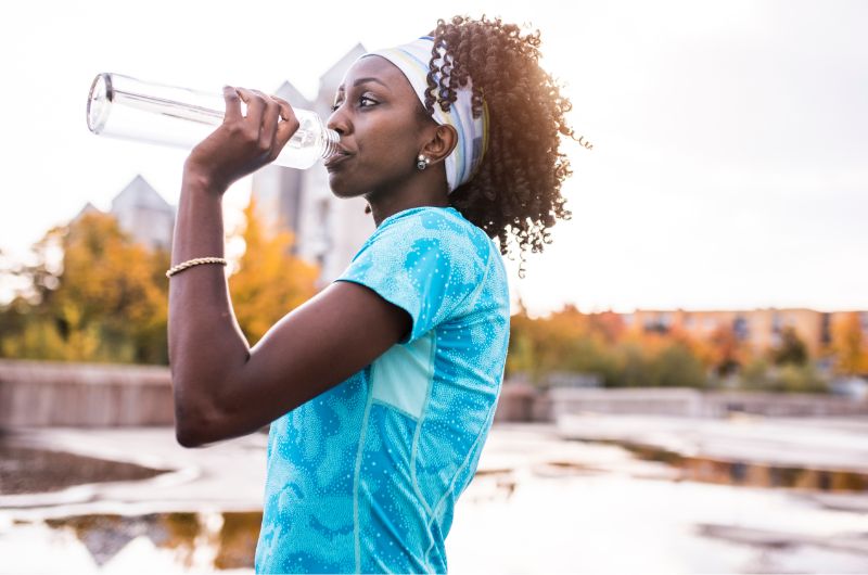 A young woman is drinking water to stay hydrated during her outdoor run