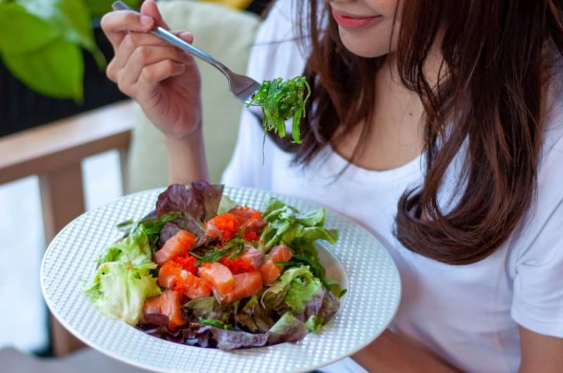 A young woman eating salad with a variety of vegetables and green leafy veggies.