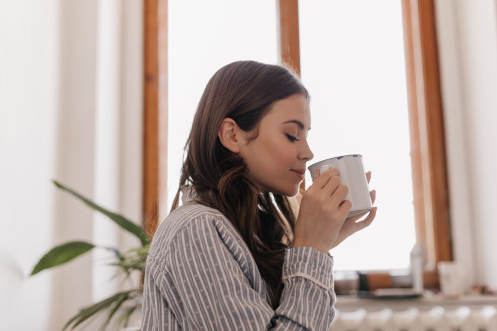 A young woman is happily enjoying her morning cup of coffee at home
