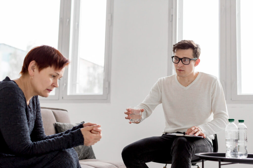 A therapist is passing a glass of water to his patient who looks noticeably anxious and sad
