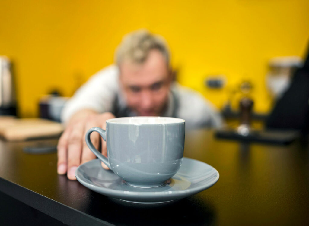 A coffee barista is looking at the cup of cappuccino that he just made