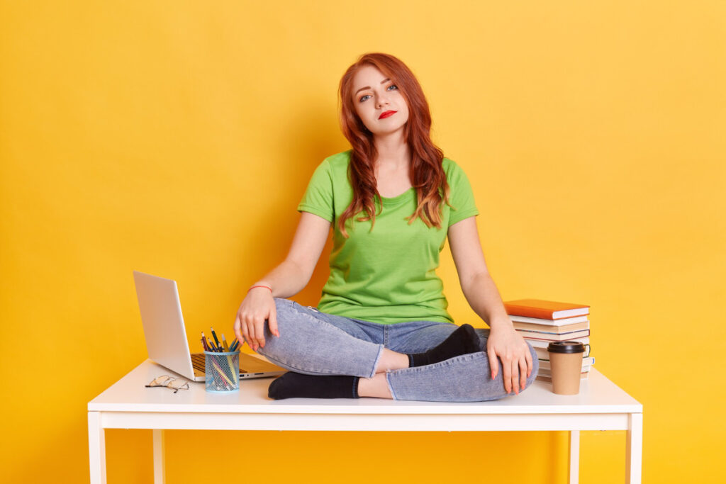 A distracted college student is sitting on her desk, not doing her schoolwork.