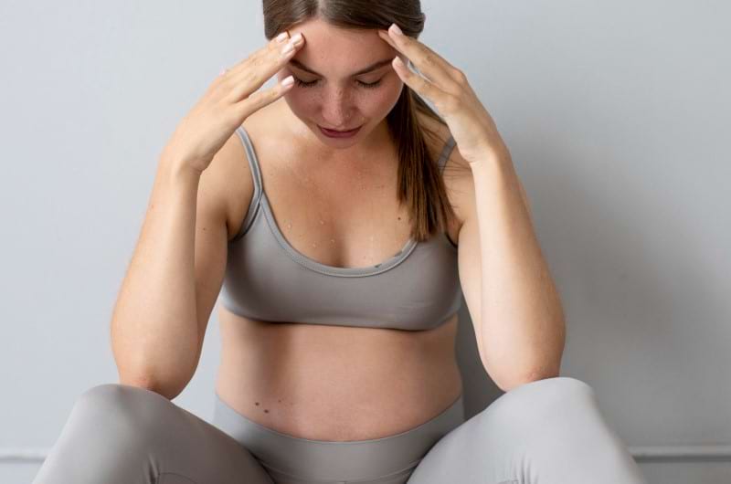 A pregnant woman sitting down on floor experiencing prenatal anxiety.