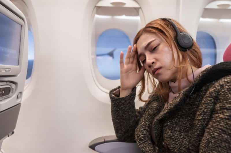 A woman sitting by the window seat in airplane is worried to look outside because of fear of flying. 
