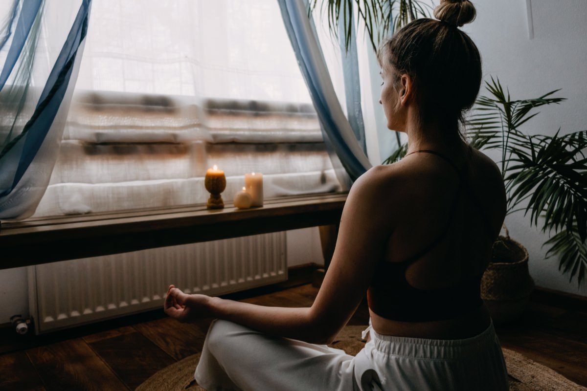 A young woman is meditating by her window as an anxiety grounding technique