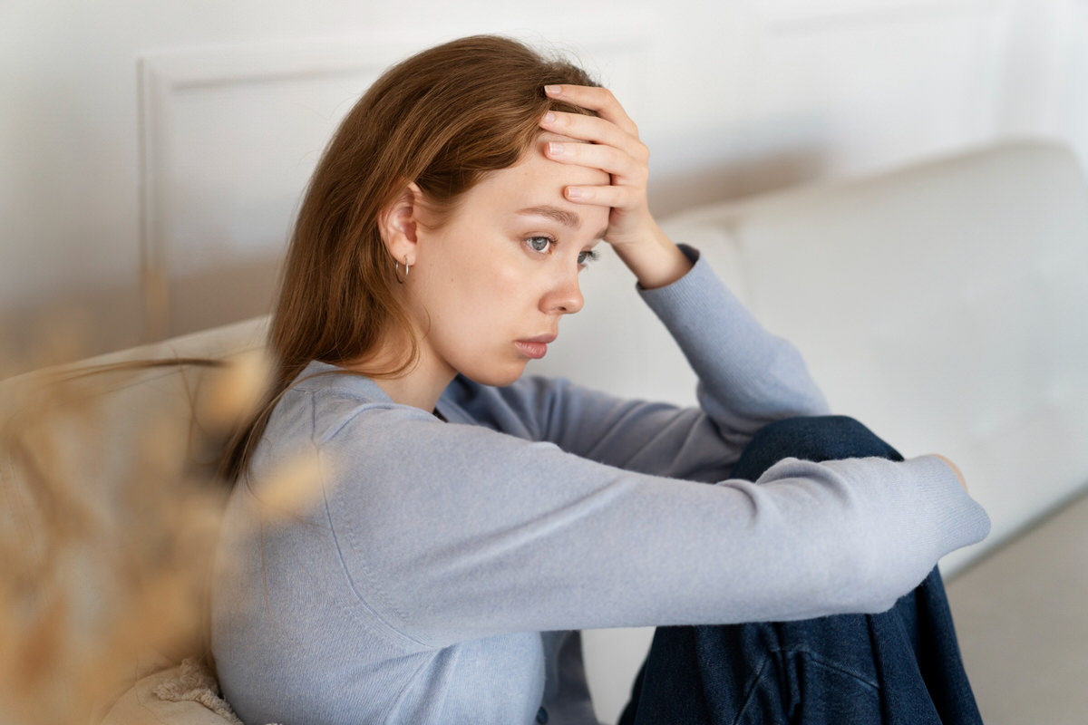 A young woman who is feeling anxious is sitting down on her sofa ruminating