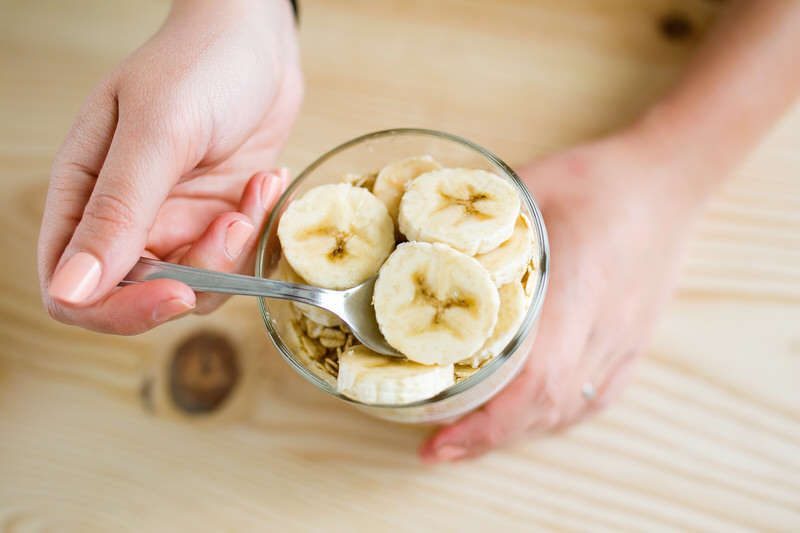 A person taking a scoop of cut-up bananas from a bowl. 