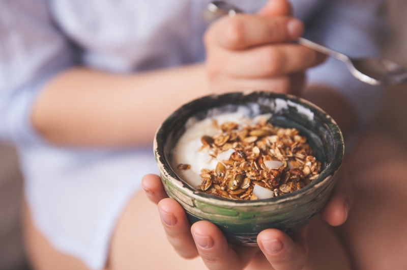 A young woman is snacking on some greek yogurt, with granola crumbles on top.