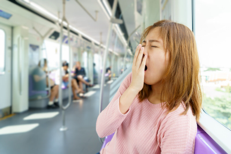 A young woman is yawning while sitting in the train.