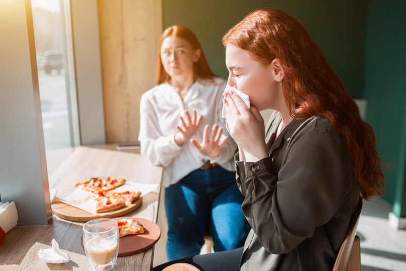 A young woman is eating pizza with spicy toppings that trigger her nose to get runny.