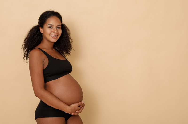 A young pregnant woman is smiling and showing off her belly.