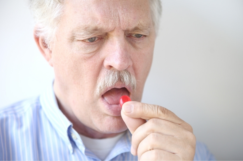 An older man is taking a cough drop to help with his sore throat.