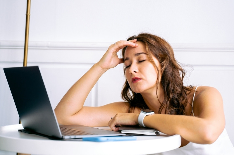 A young woman is working on her laptop and feeling fatigue, possibly because she has low iron levels.