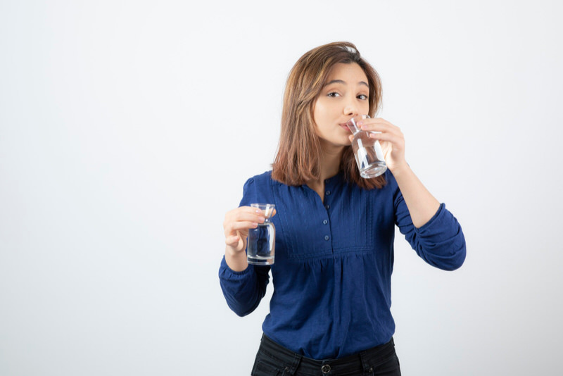 A young girl is holding 2 cups of water and drinking out of one of them to catch up on her daily water intake goal.