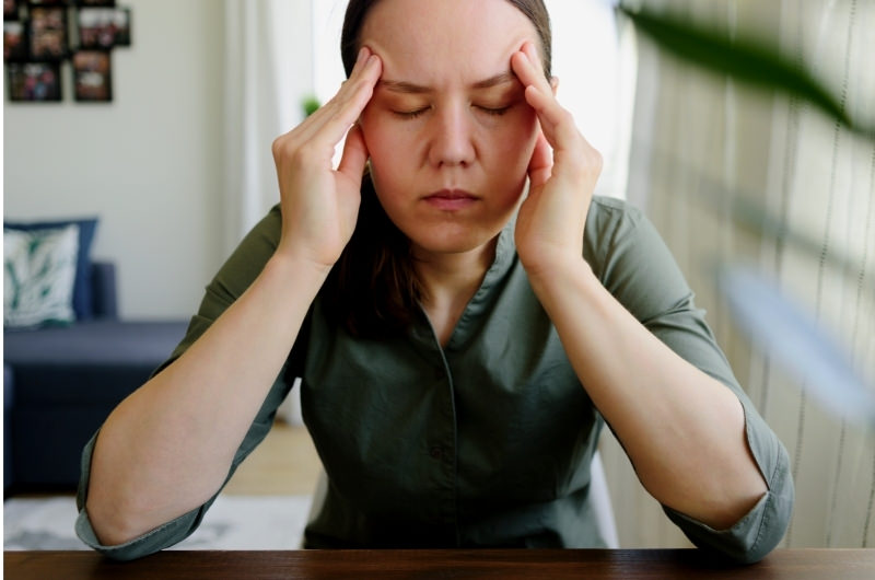 A woman is rubbing the sides of her head with her hands because she is stressing out.