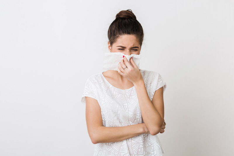 A woman with the common cold is blowing her nose to get rid of mucus