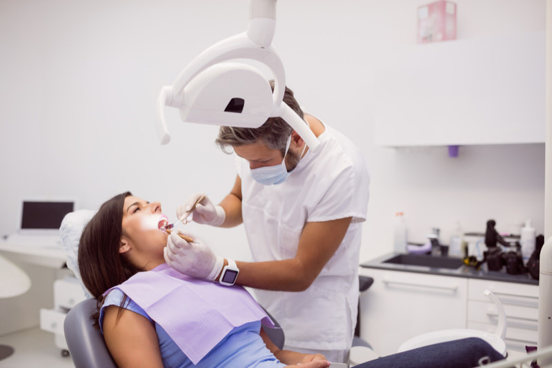 A dentist is examining his patient's dry socket on her wisdom tooth.