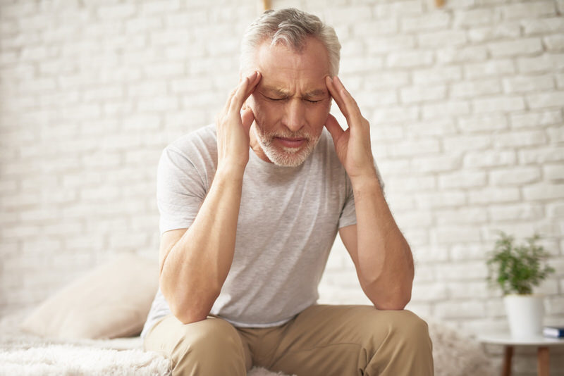 An older man who is having a migraine is sitting down for a bit because his vision has also been affected.