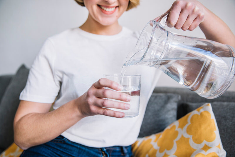 A young woman is pouring a small amount of water into a glass to prevent drinking too much water and bloating.