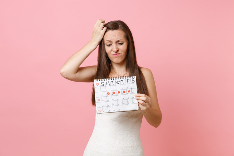 A young woman on her period is frustrated as she looks at a calendar where she logs her period cycle.