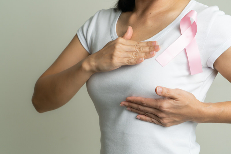 A woman holding the top and bottom of her left breast with a pink ribbon above to signify breast cancer awareness.