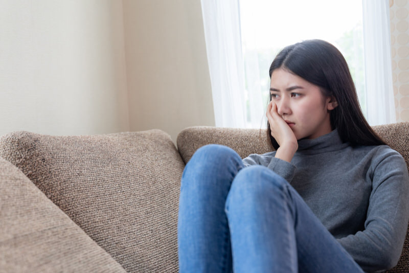 A young woman is sitting on the sofa looking sad and depressed