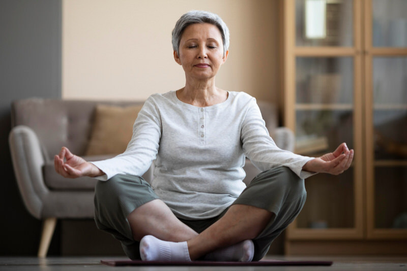 An older woman is meditating to help reduce her recent increase in stress and anxiety