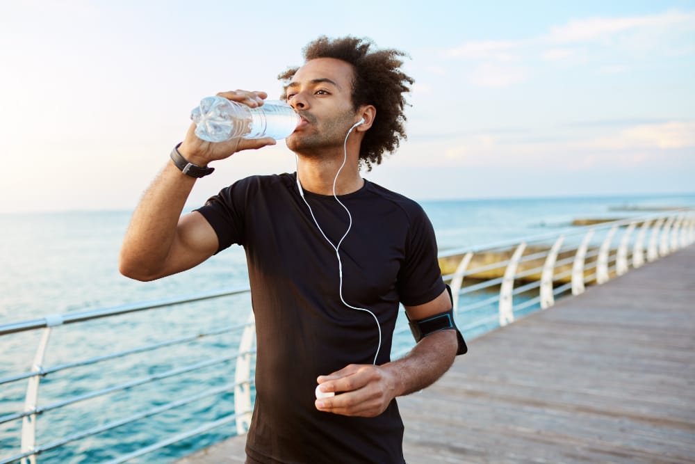 A man is taking a break to drink water and stay hydrated while he's running to stay fit