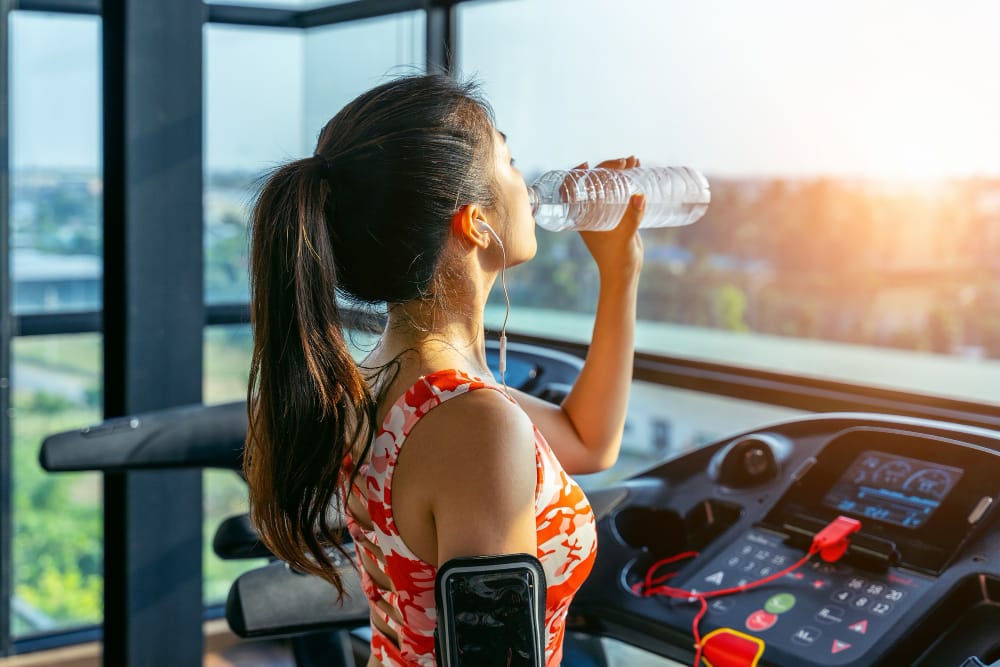 A young woman has some water with EAAs in it during a walk on the treadmill