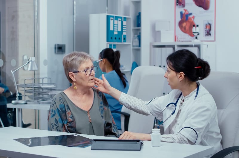 An older female patient has her doctor examine her recent neck pain to see if it could have been caused by a ruptured aneurysm