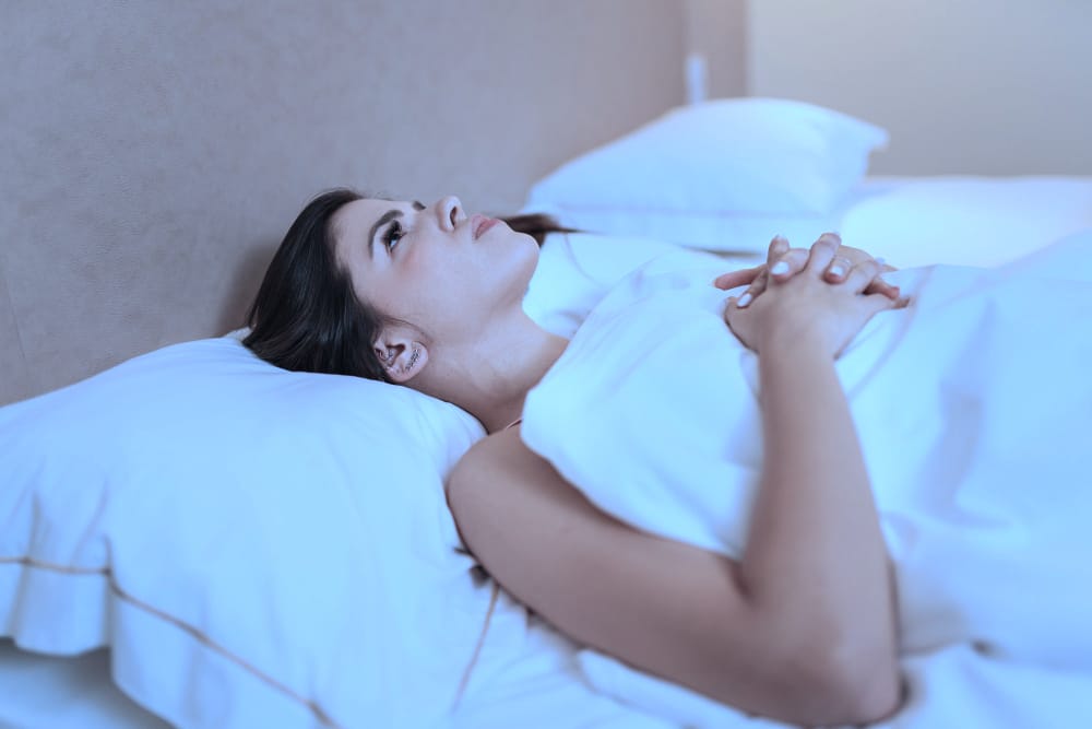 A sleepless woman is lying in her bed late at night, unable to fall asleep