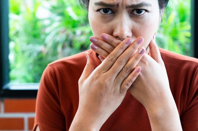 A woman is holding her mouth after feeling bile reflux