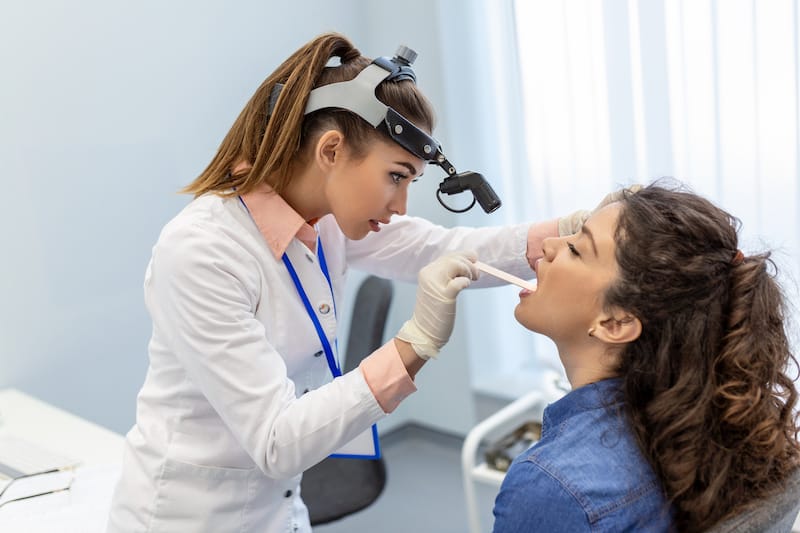 A throat doctor is checking her patients tonsils to see if they need to be surgically removed