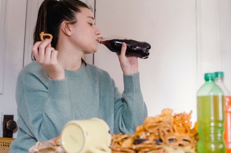 A young woman is eating lots of junk food and drinking soda, leading her to have a possible panic attack after