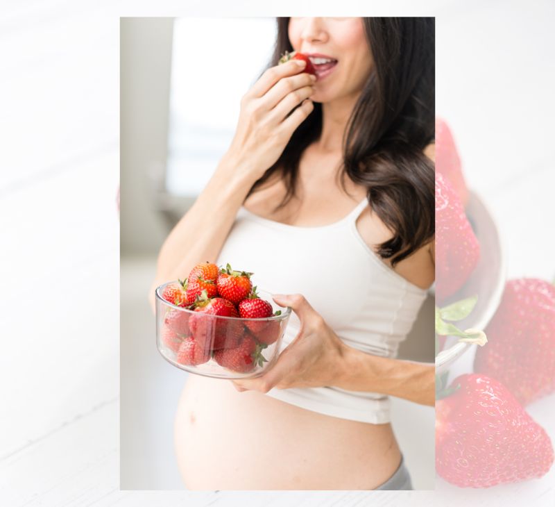 A pregnant woman is happily eating a large bowl of strawberries