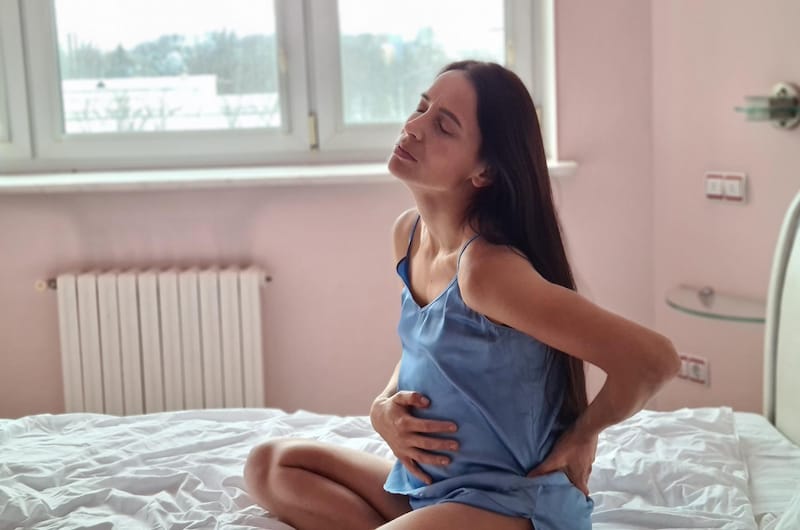 A pregnant woman is sitting up on her bed feeling unwell because of her diverticulitis condition
