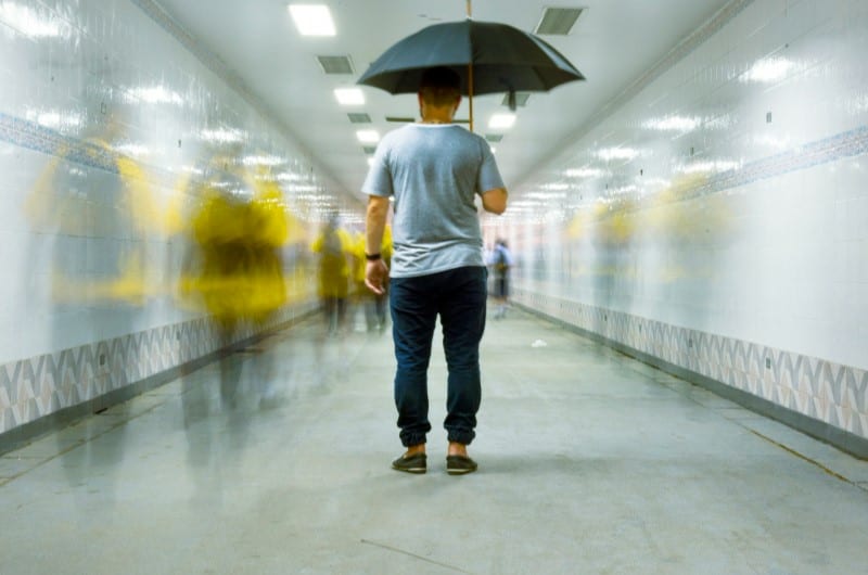 A man is walking with an umbrella, lost in thought due to anxiety, unable to focus on his surroundings.