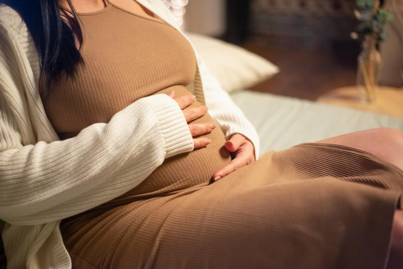 A pregnant woman is sitting down touching her pregnant belly where her baby is actively moving in the womb