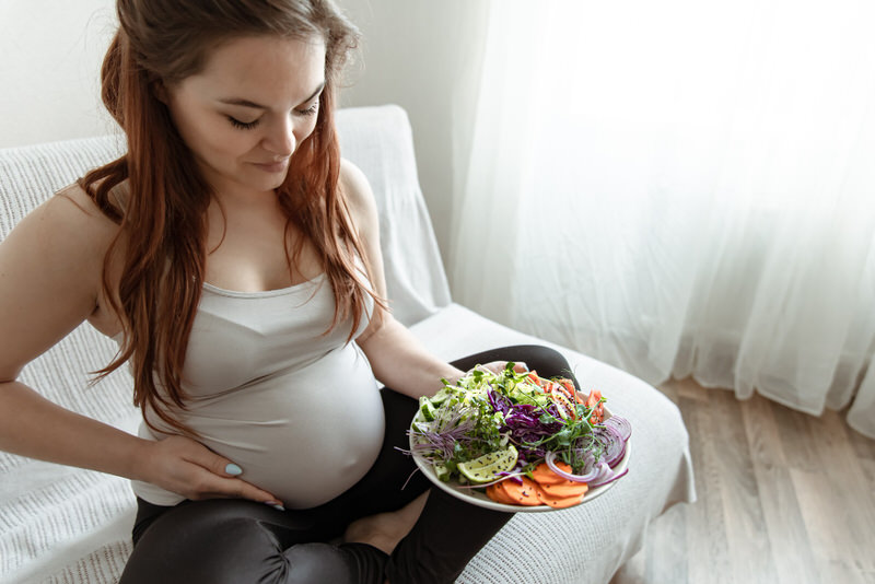 A pregnant woman is holding a large salad that she's about to eat for lunch