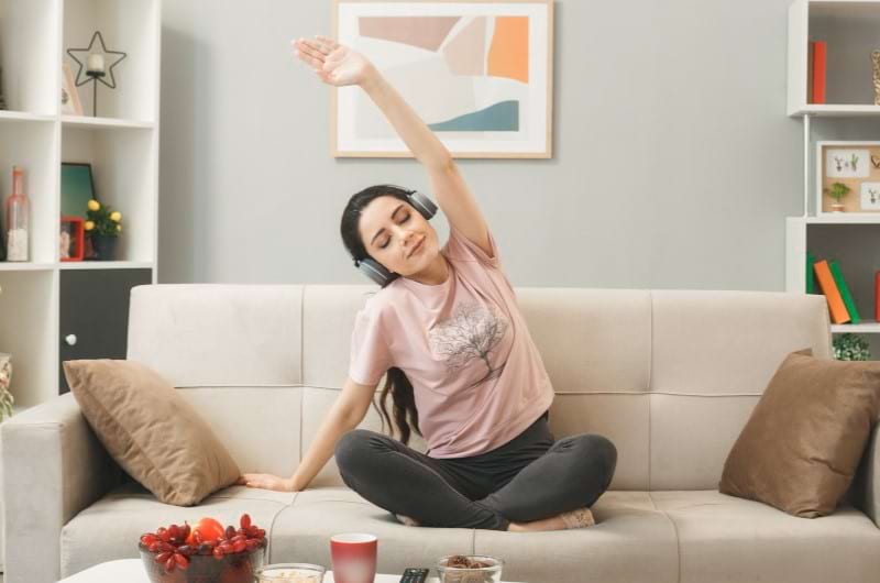 A woman stretching on sofa while listening to music to manage her anxiety. 