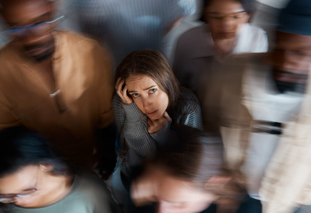 A young woman is shown looking noticeably stressed and anxious among a crowd of people in a social setting